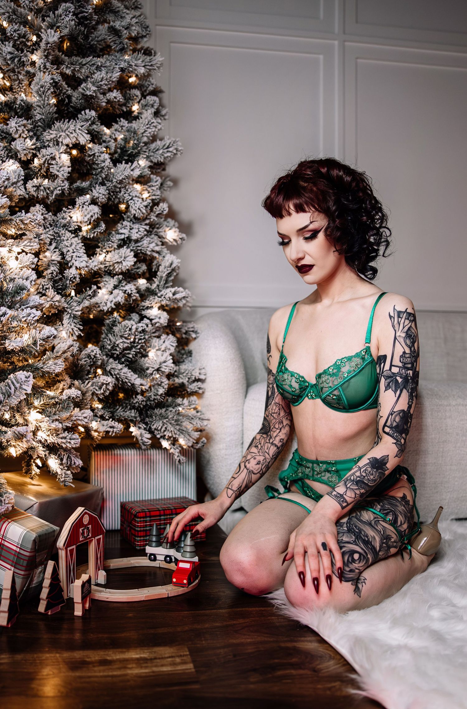 Holiday themed boudoir photo with decorated Christmas tree and emerald lingerie set on plaid blanket.