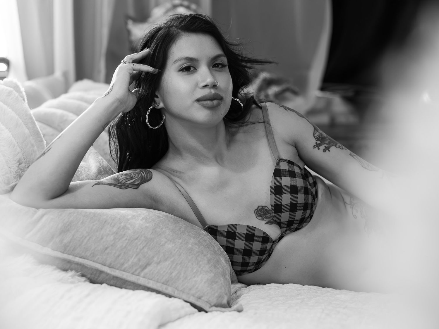 A black and white photograph shows a woman in a plaid top reclining on a couch with pillows.