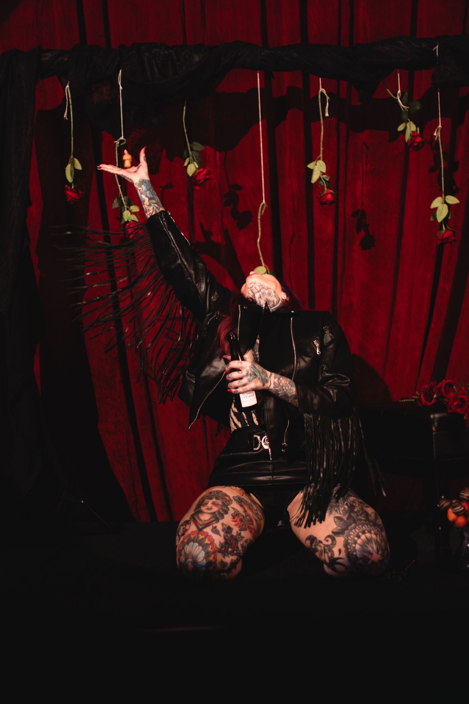 Dark moody performance shots against red velvet curtains with hanging decorative elements.