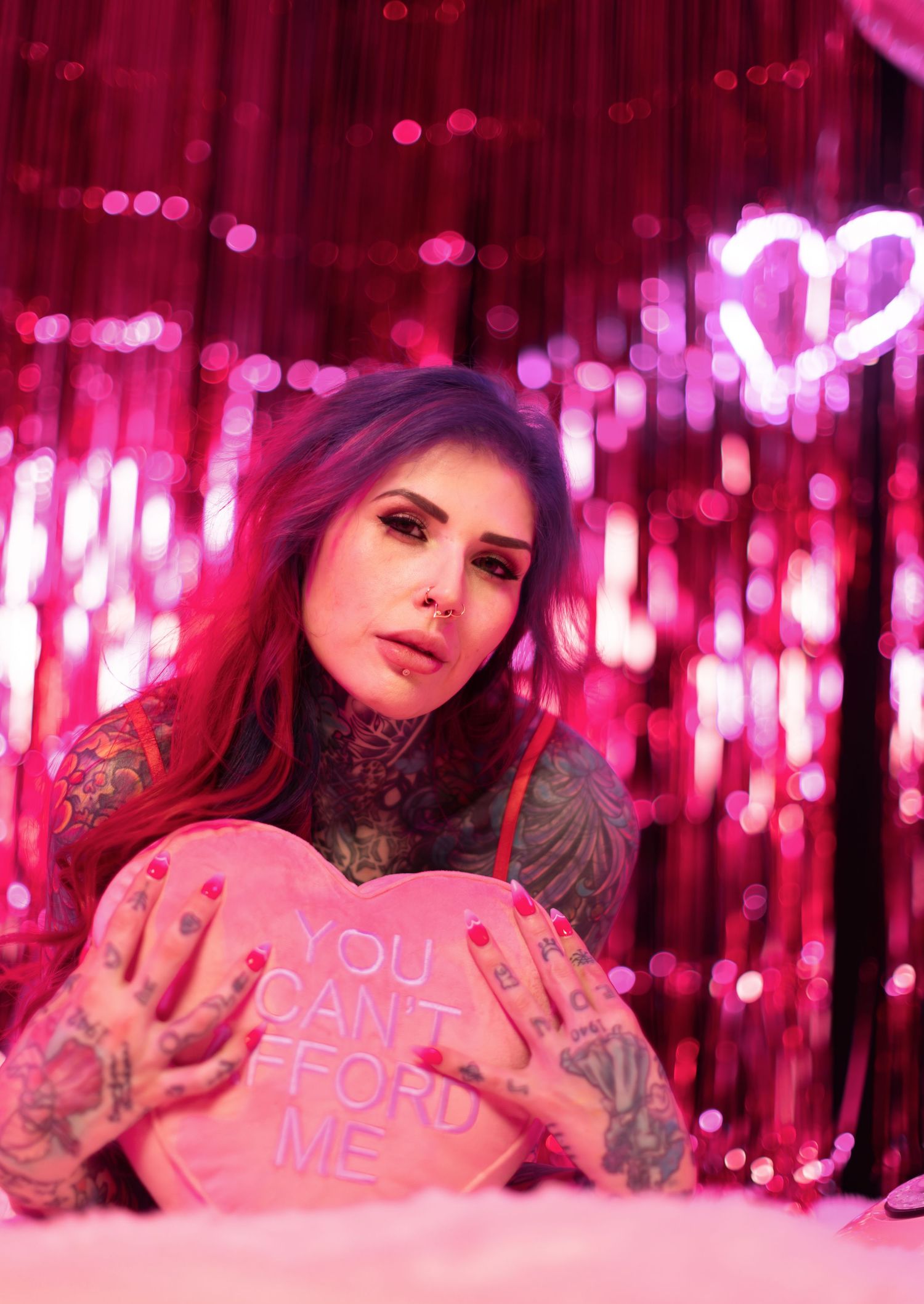 Model poses with pink heart-shaped decorations against sparkly pink backdrop with tinsel.