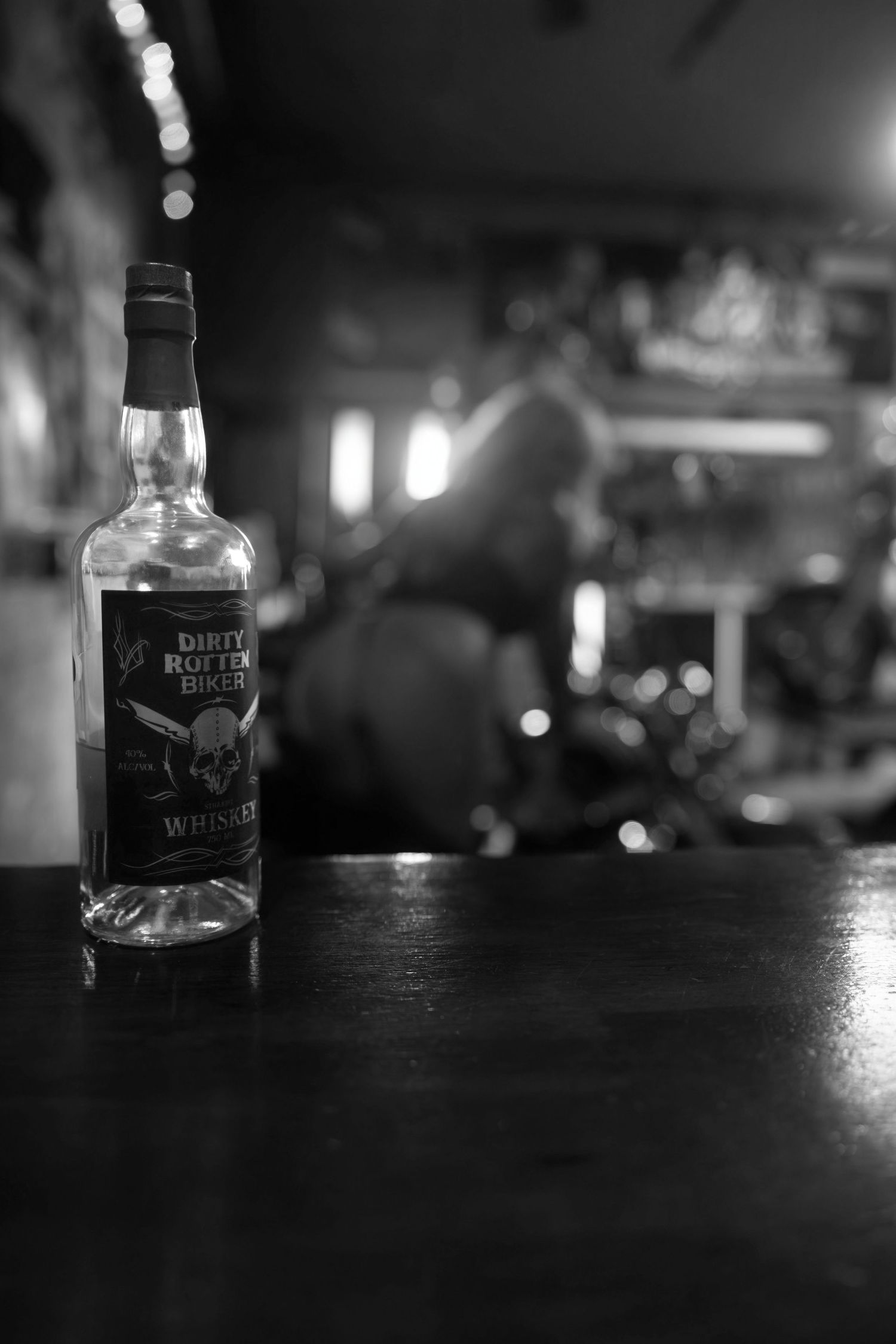 Black and white photography of whiskey bottles on a dark bar counter.