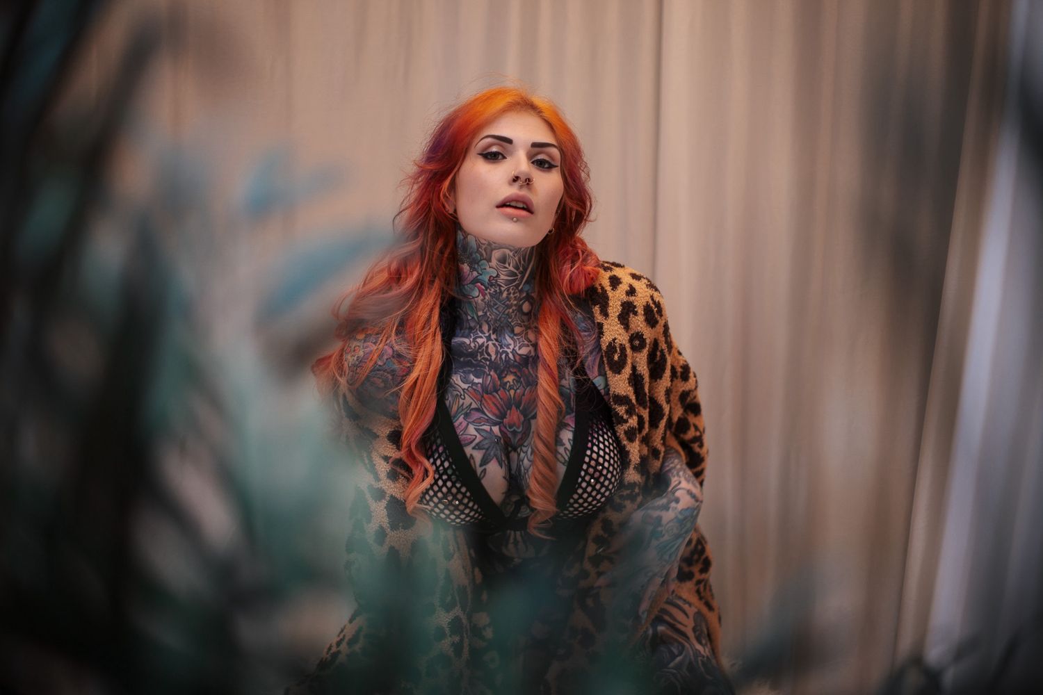 A person with vibrant red hair poses in a black lace dress against a neutral background.