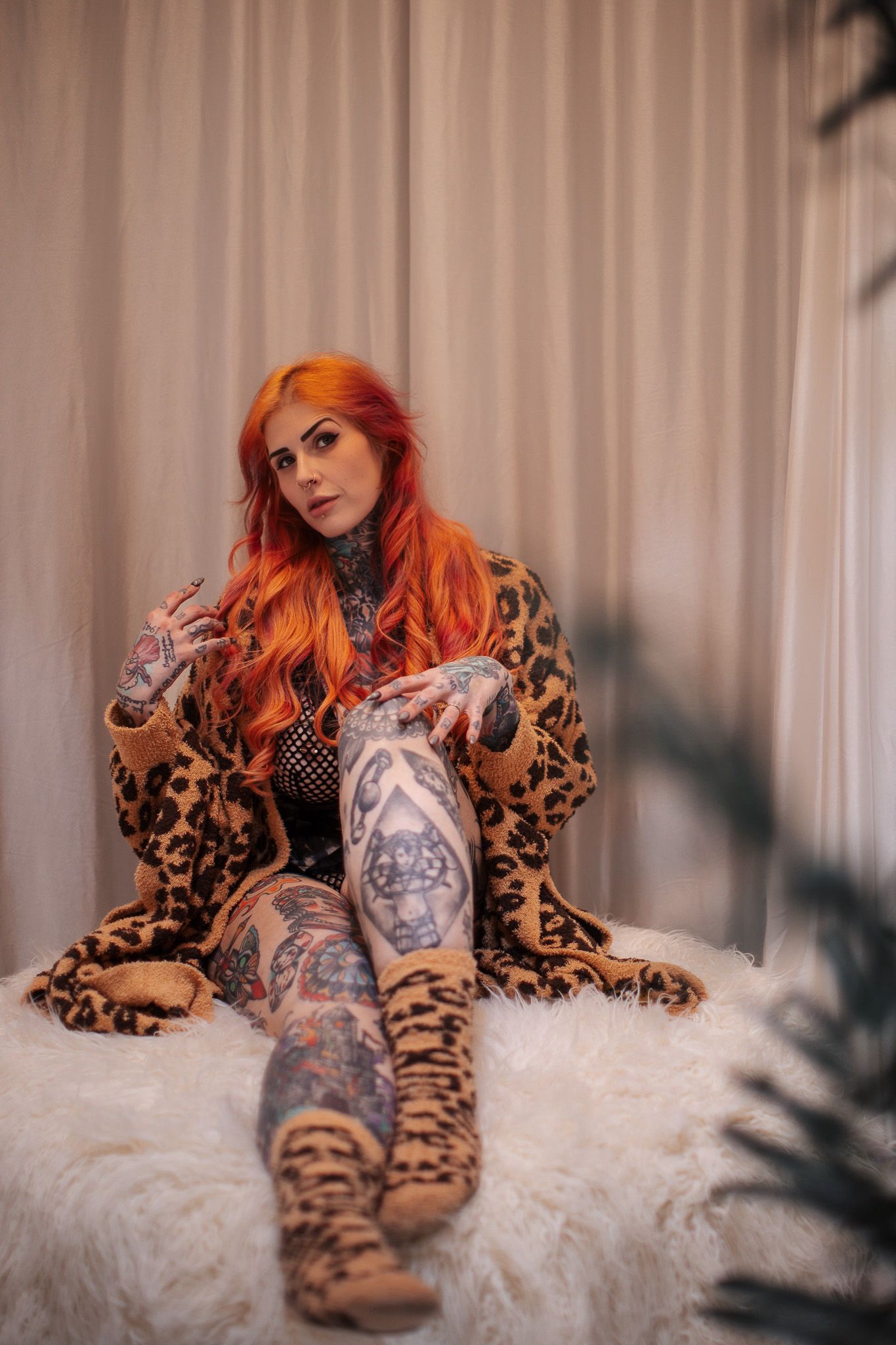 Model with bright orange hair poses on white fur wearing leopard print and showing tattoos in artistic photo series.