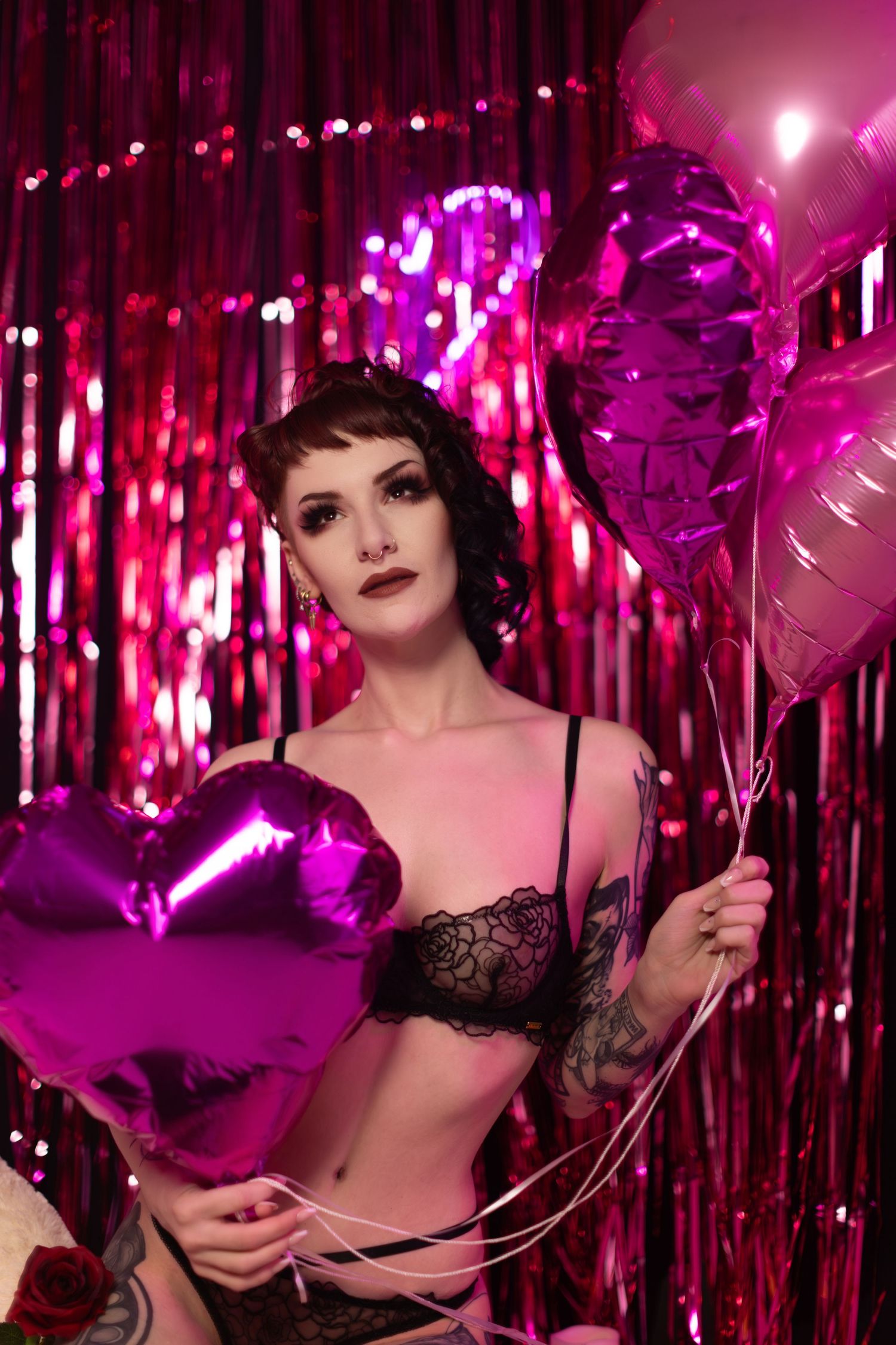 Burlesque-style performer poses with props against sparkly pink curtain backdrop in theatrical lighting.