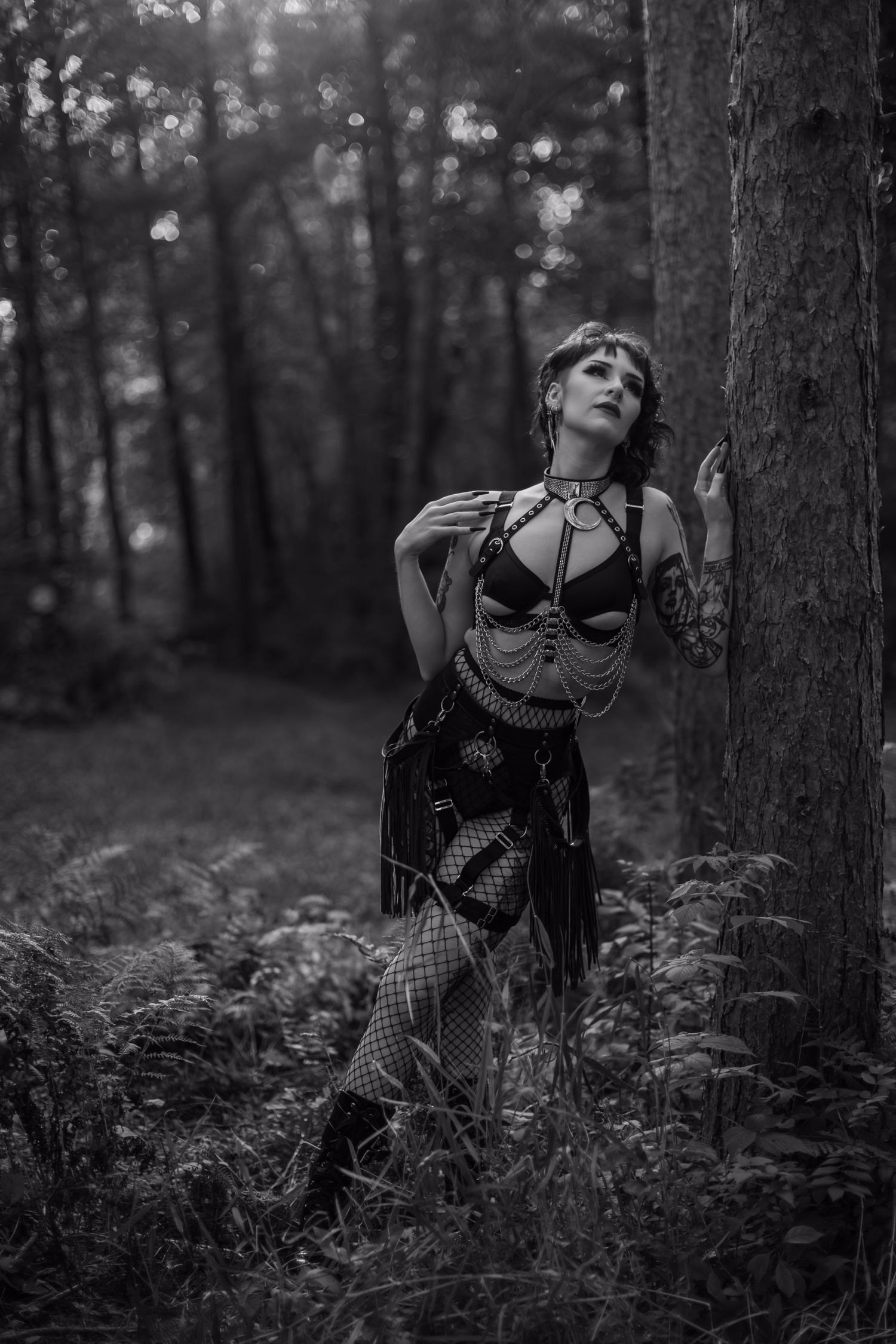 Moody black and white portrait in forest setting with dramatic pose and gothic styling.
