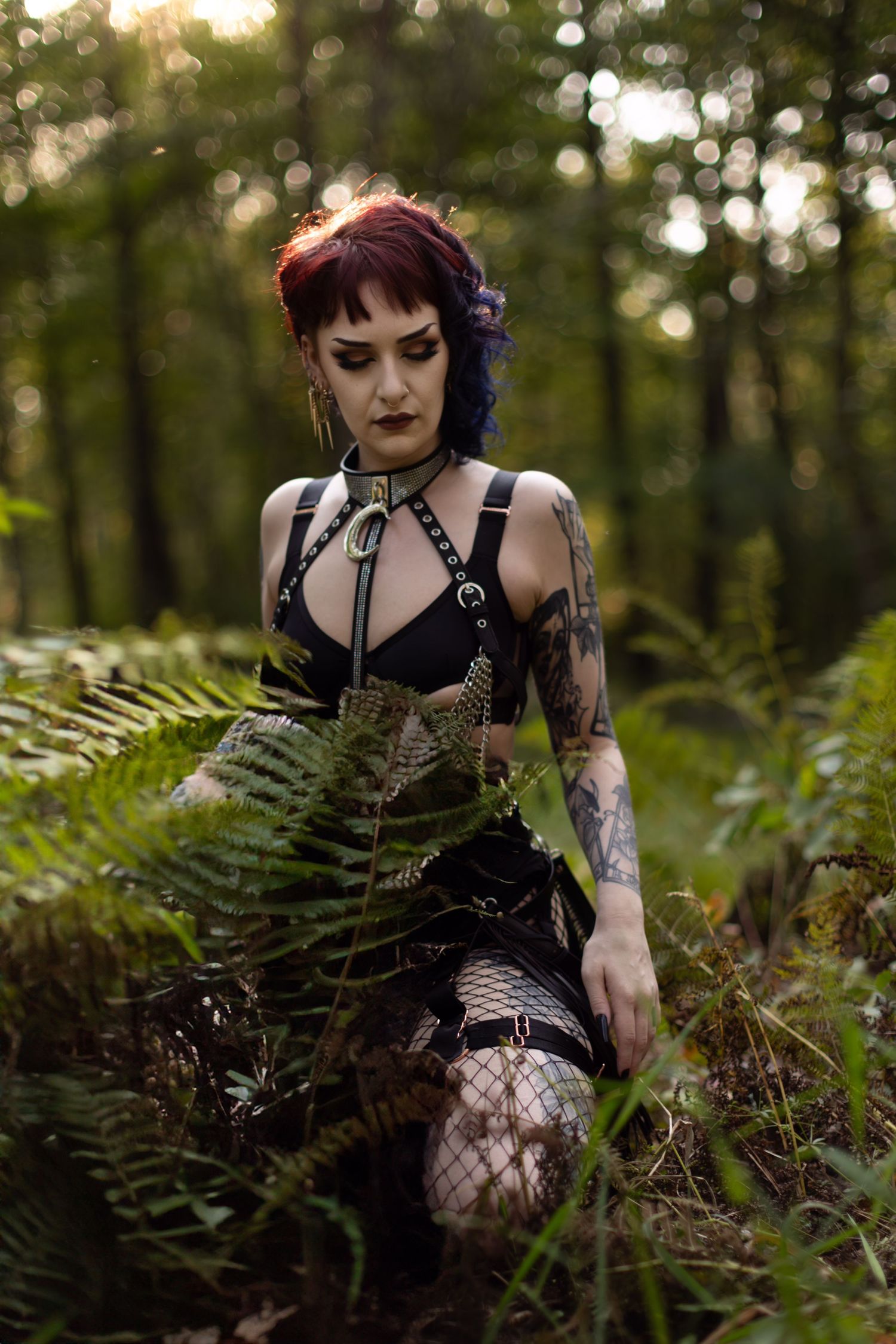 Alternative model poses among wild ferns wearing black gothic attire and fishnet accessories.