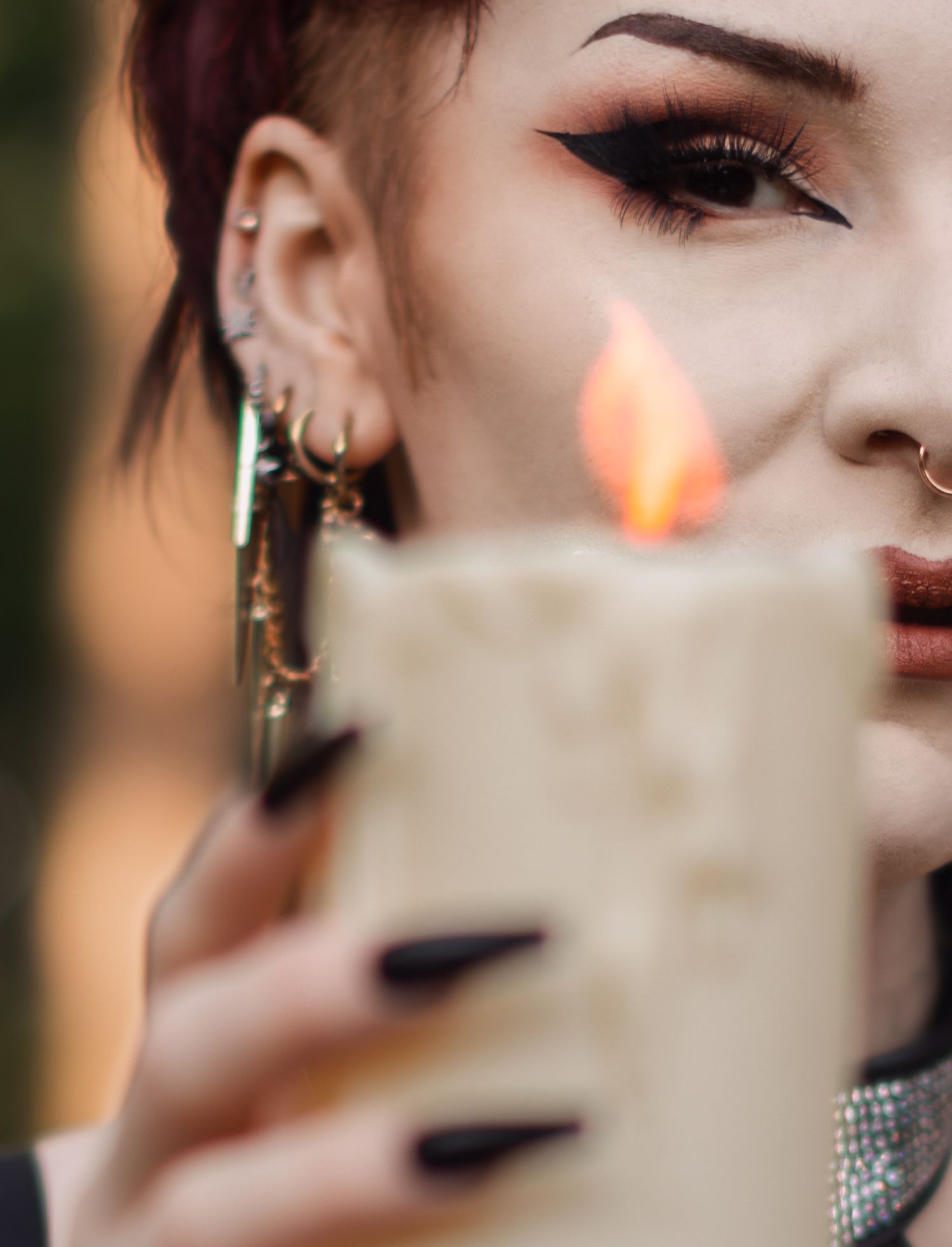 Close-up shot showing dramatic eye makeup and multiple ear piercings with lit candle.