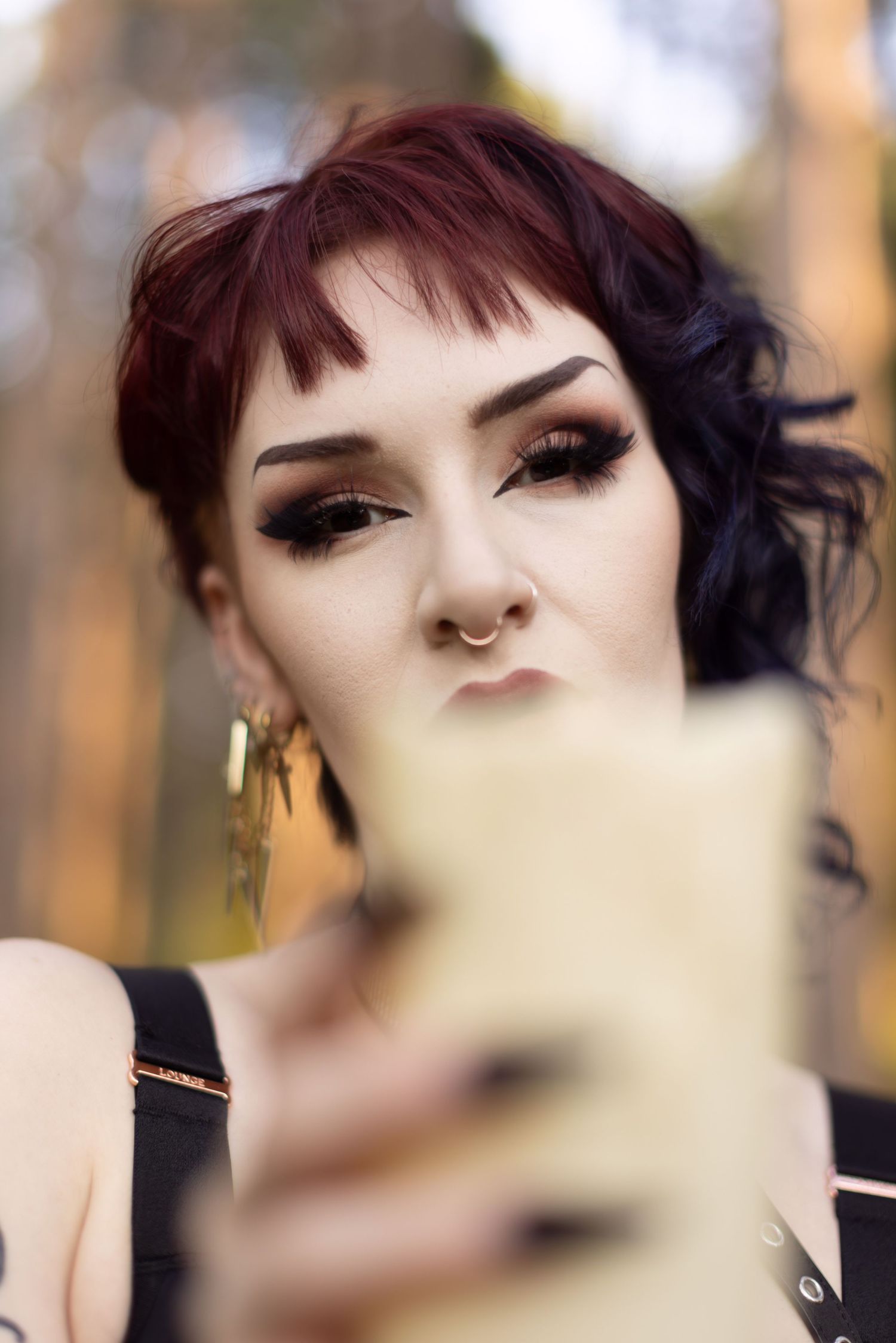 Gothic fashion model poses dramatically in a forest setting with dark makeup and red hair.