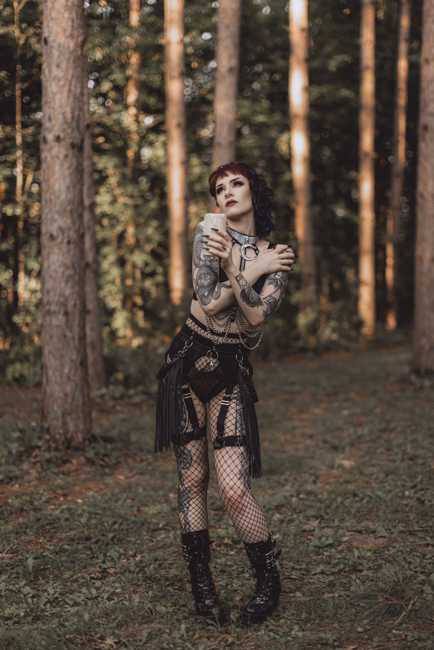 Gothic styled figure in mesh outfit poses dramatically against forest backdrop.