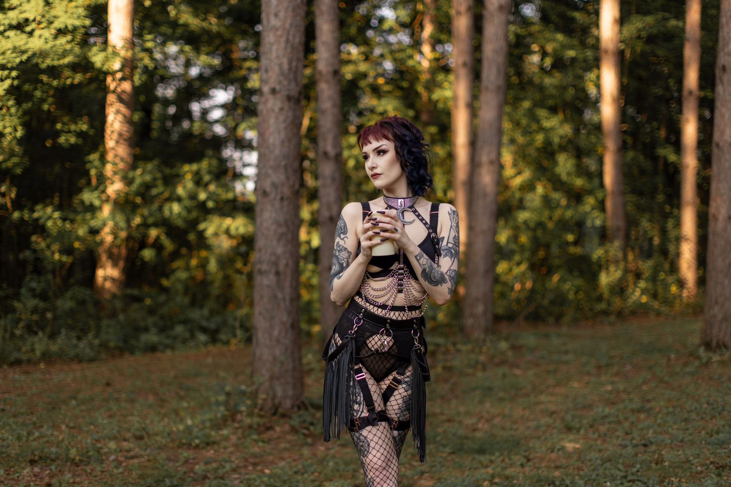 Alternative model in gothic attire walking through pine forest at sunset.