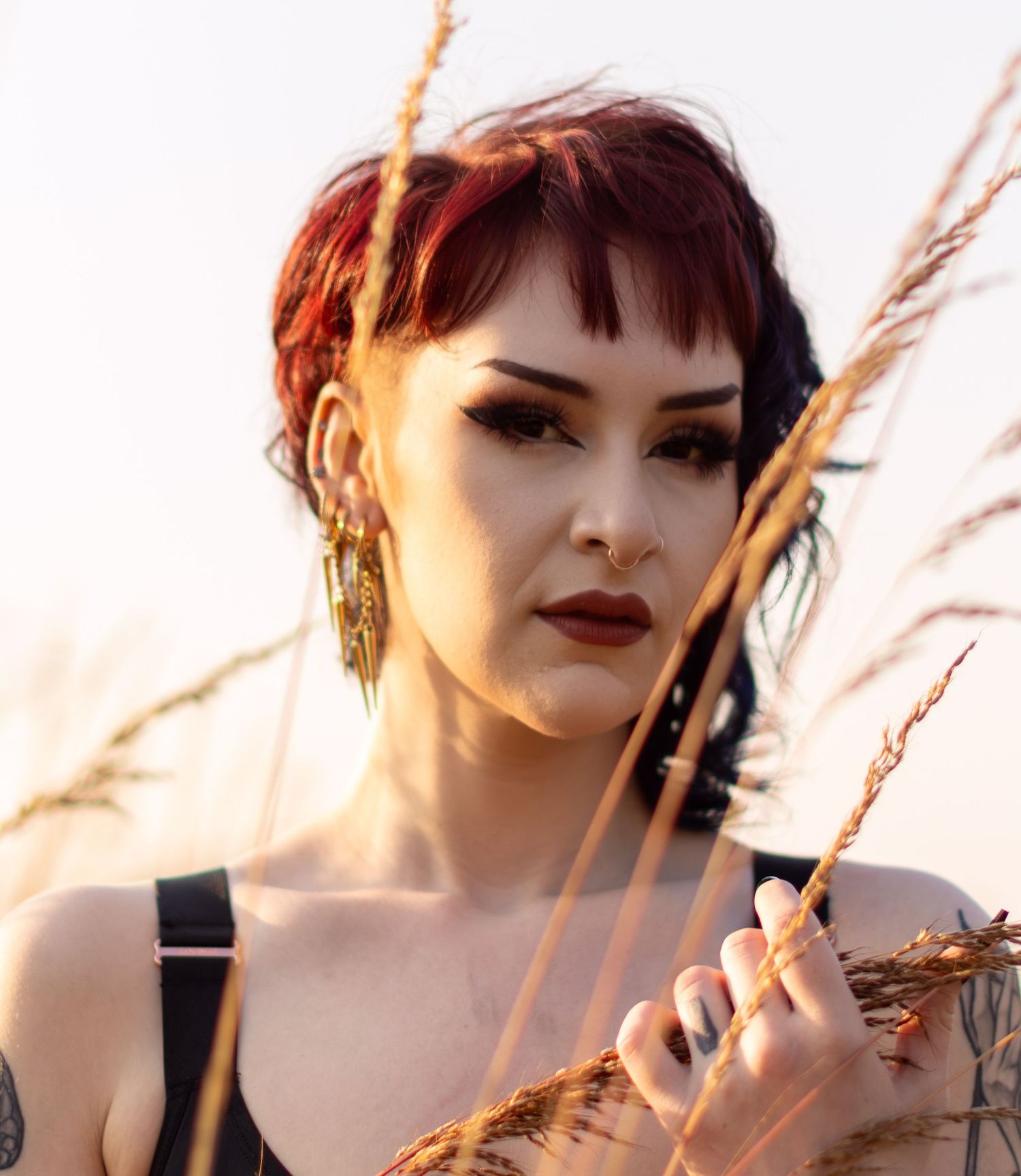 Close-up portrait with wheat stalks and dramatic makeup in warm sunset lighting.