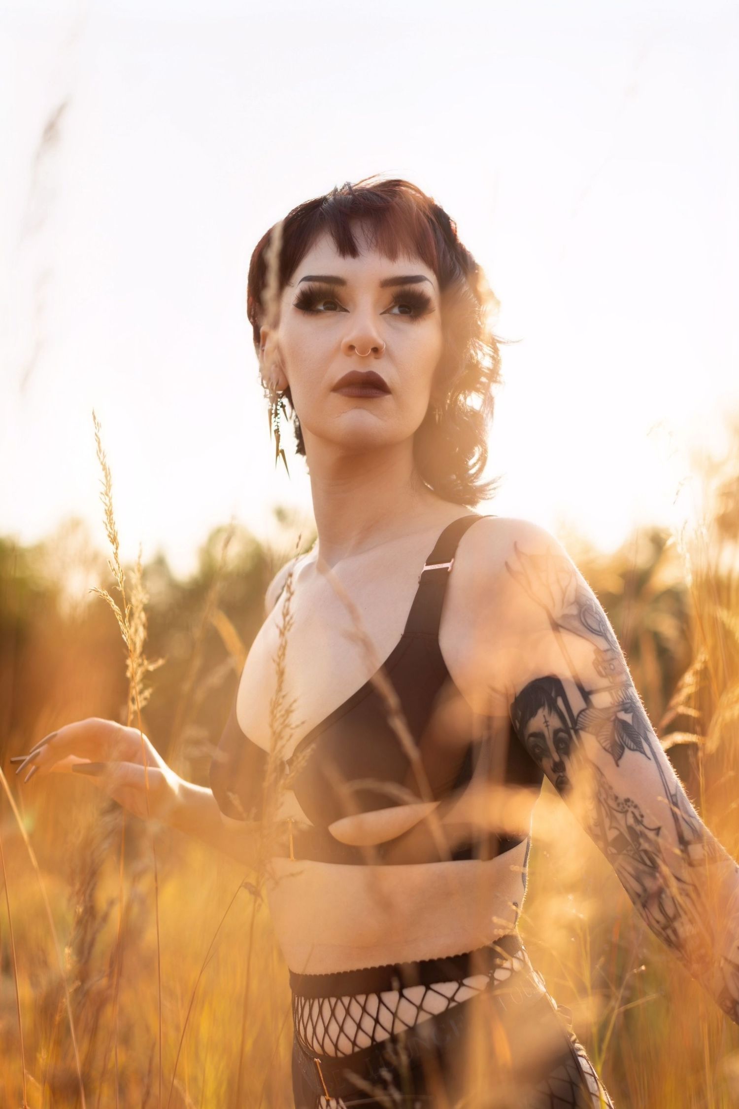 Alternative model in black crop top poses among tall wheat stalks at sunset.