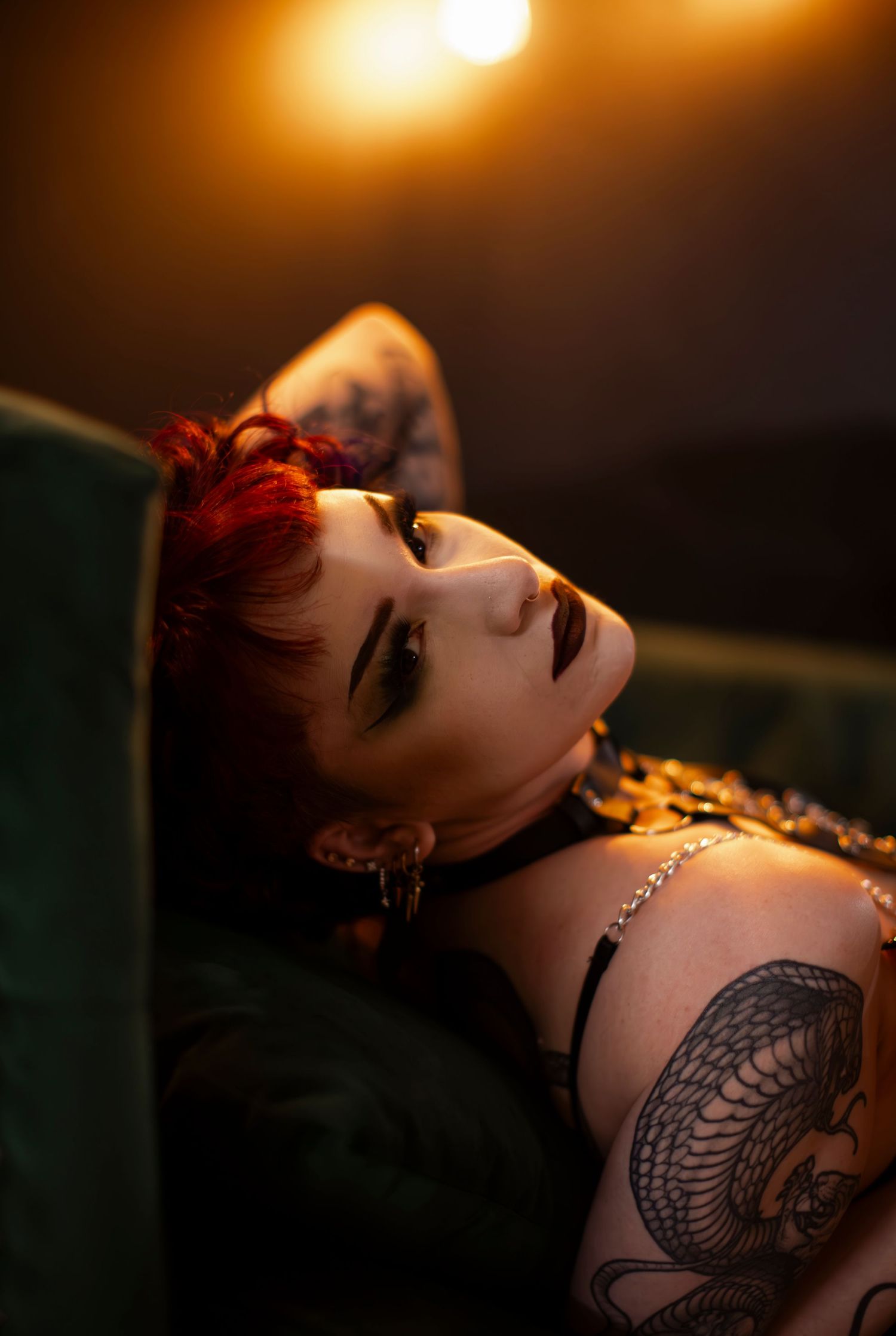 Moody portrait of tattooed woman with red hair in dramatic lighting.
