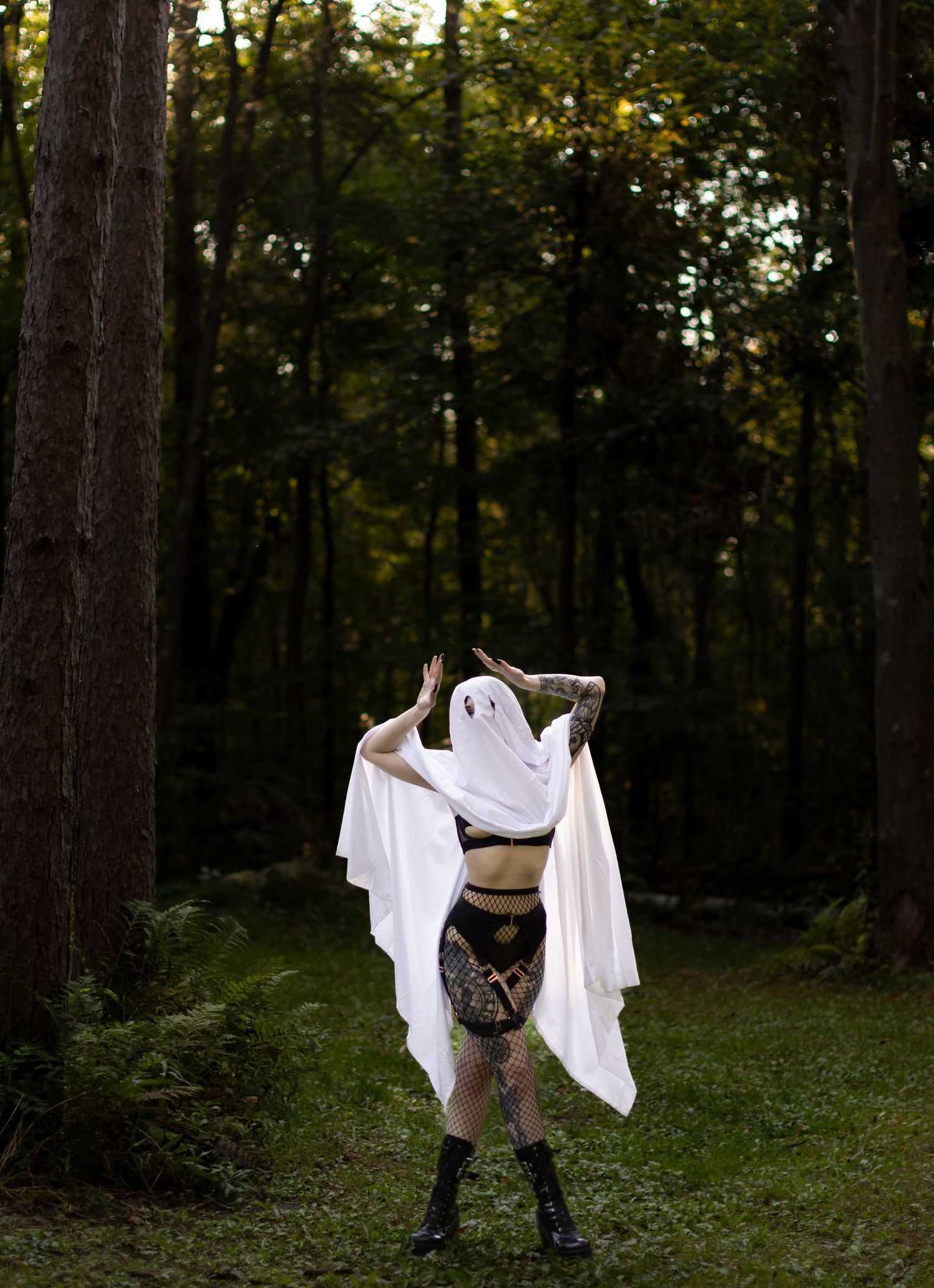 Playful ghost costume with gothic accessories stands in moody forest setting.