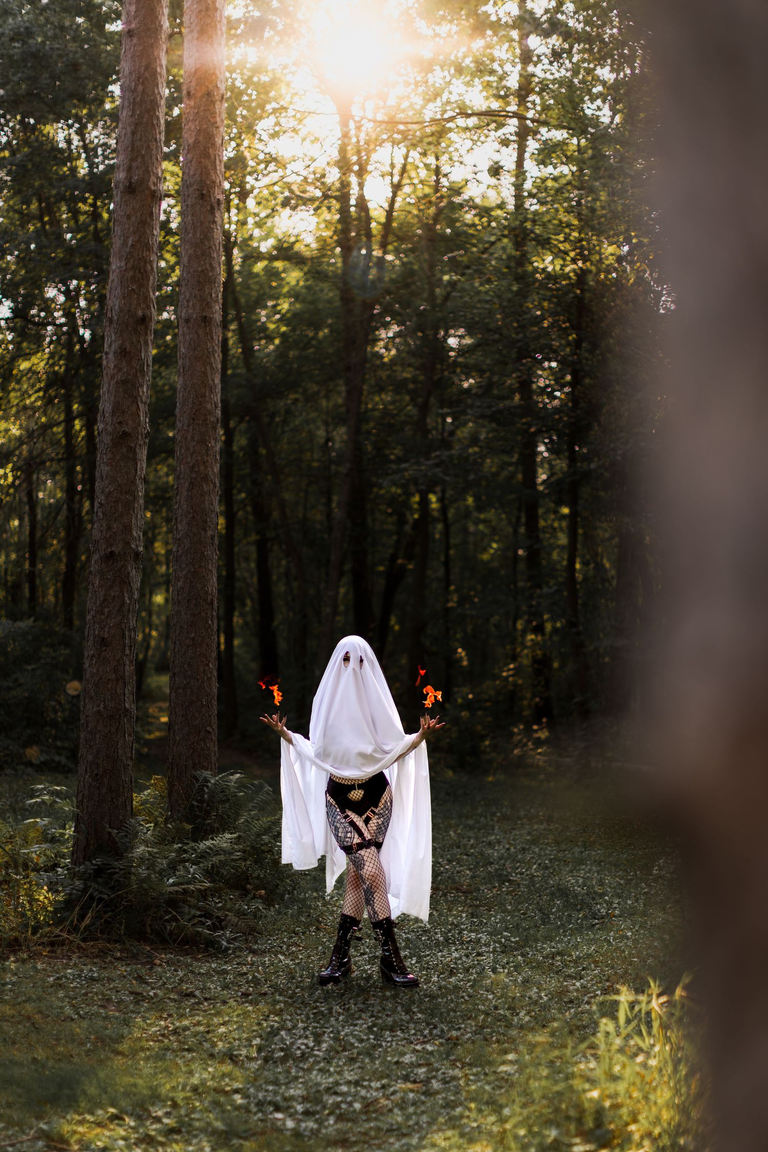 Ghostly figure holding red candles poses in sun-dappled forest clearing.