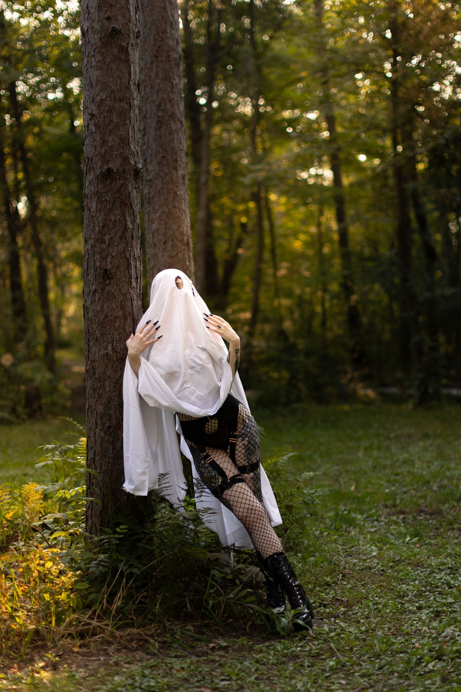 Ghost in gothic attire leans dramatically against tree trunk in forest setting.