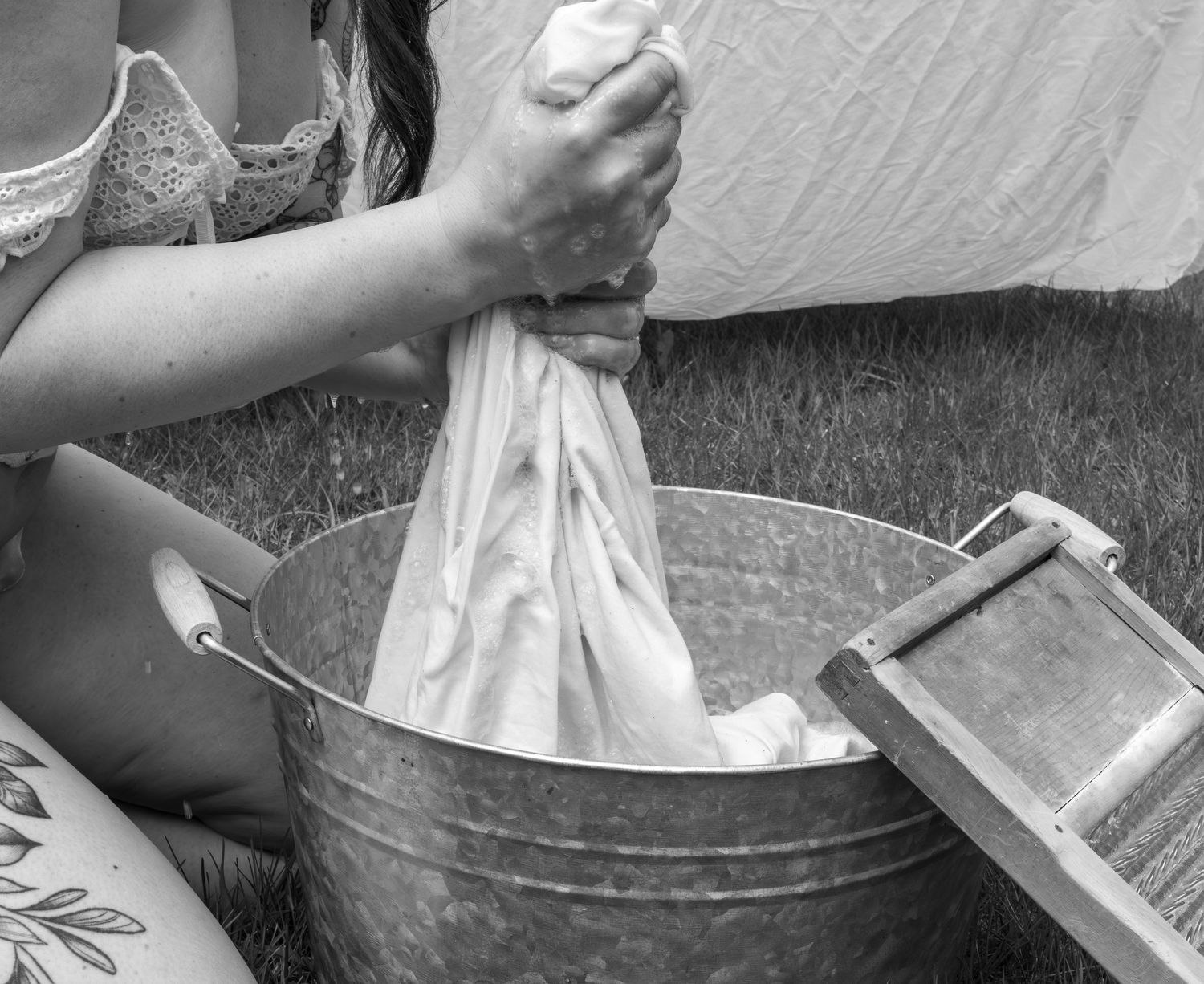 Hands washing fabric in vintage metal washtub outdoors.
