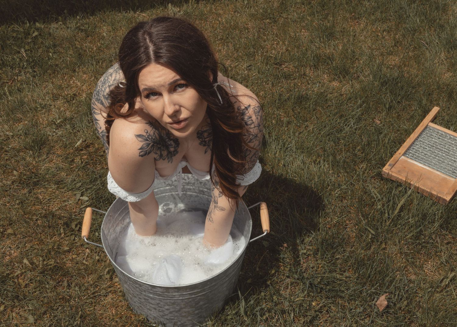 Person in vintage dress doing laundry with metal washtub outdoors.