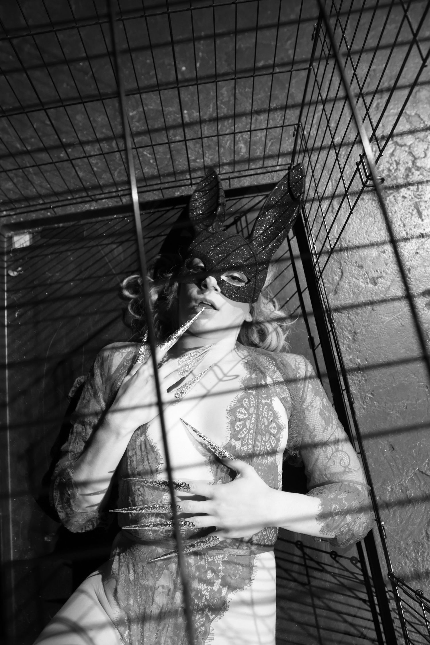 Artistic black and white portrait through metal cage bars showing shadows and texture.