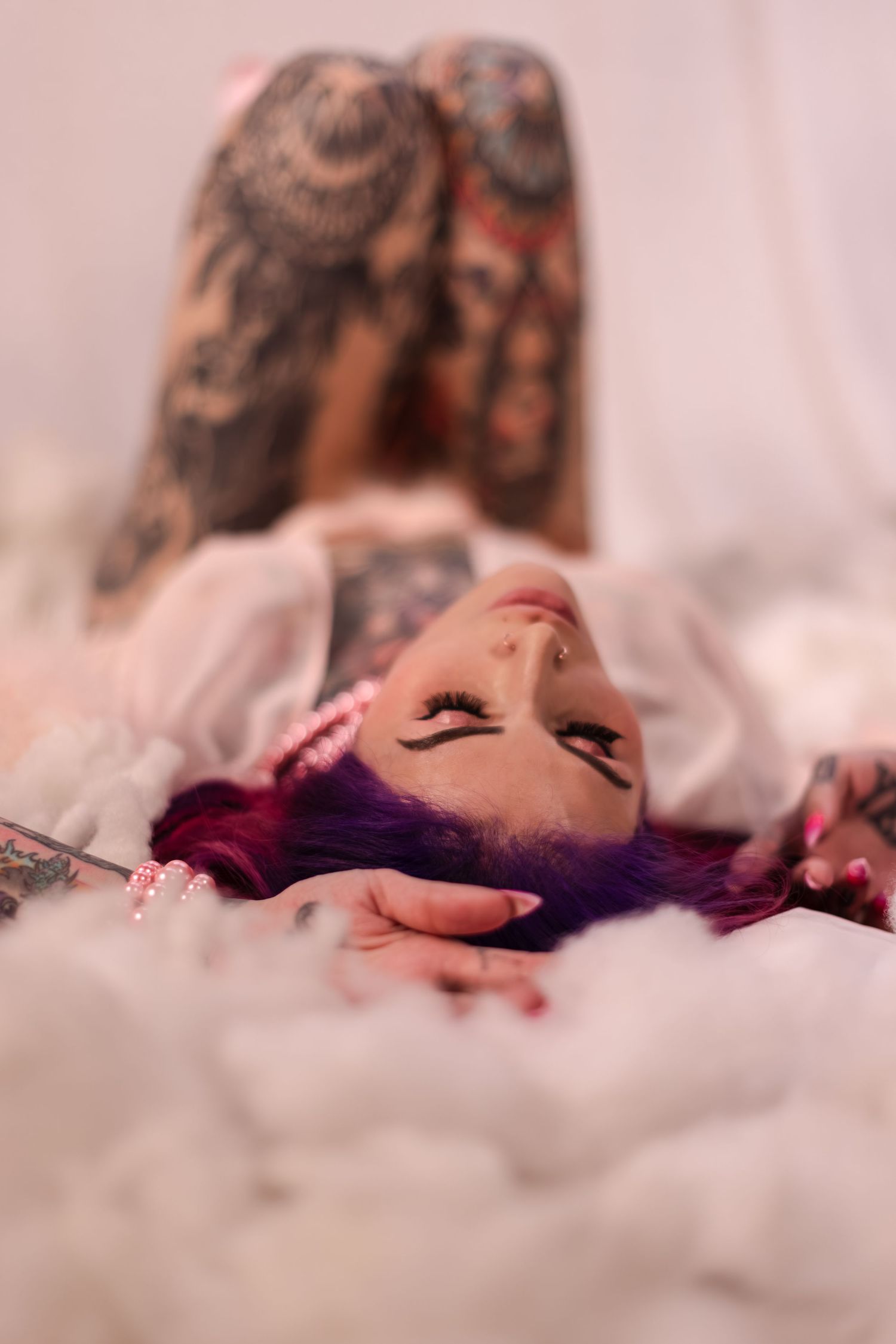 Artistic boudoir photo showing figure reclining on white bedding with red hair.