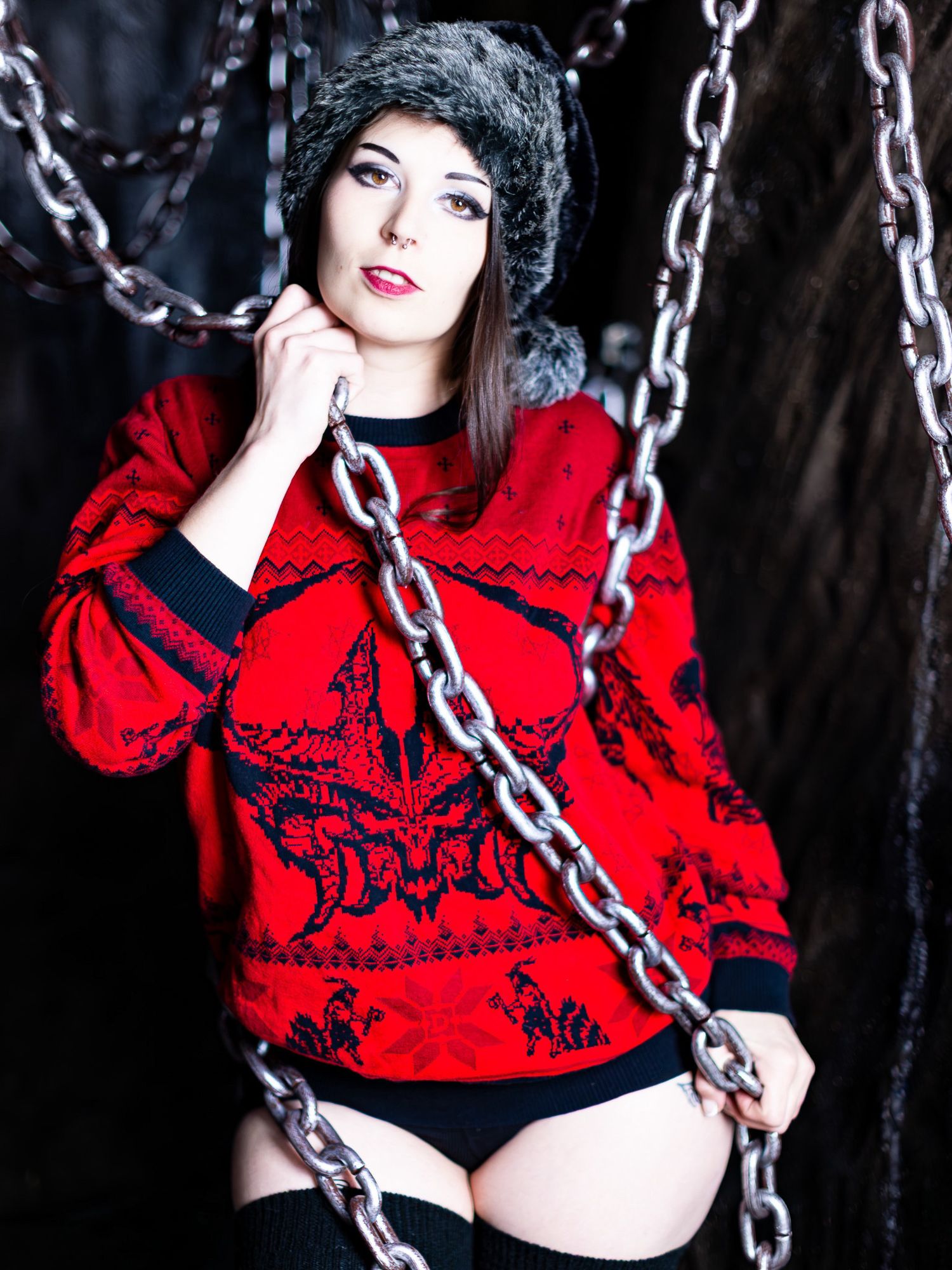 Gothic fashion model in bright red sweater poses dramatically with metal chains against dark background.