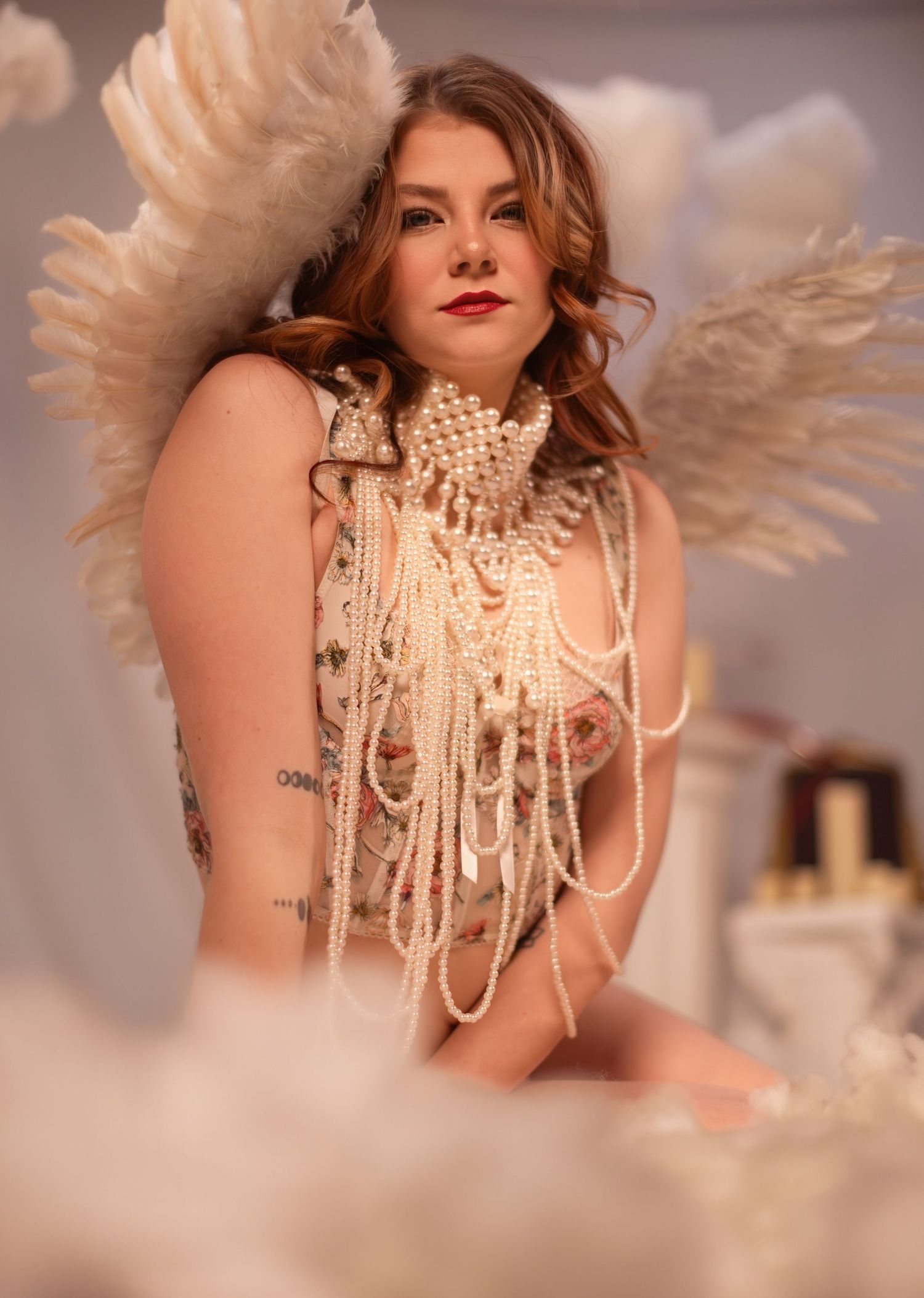 A model wearing cream pearls and feathered wings in a glamorous boudoir style photoshoot.