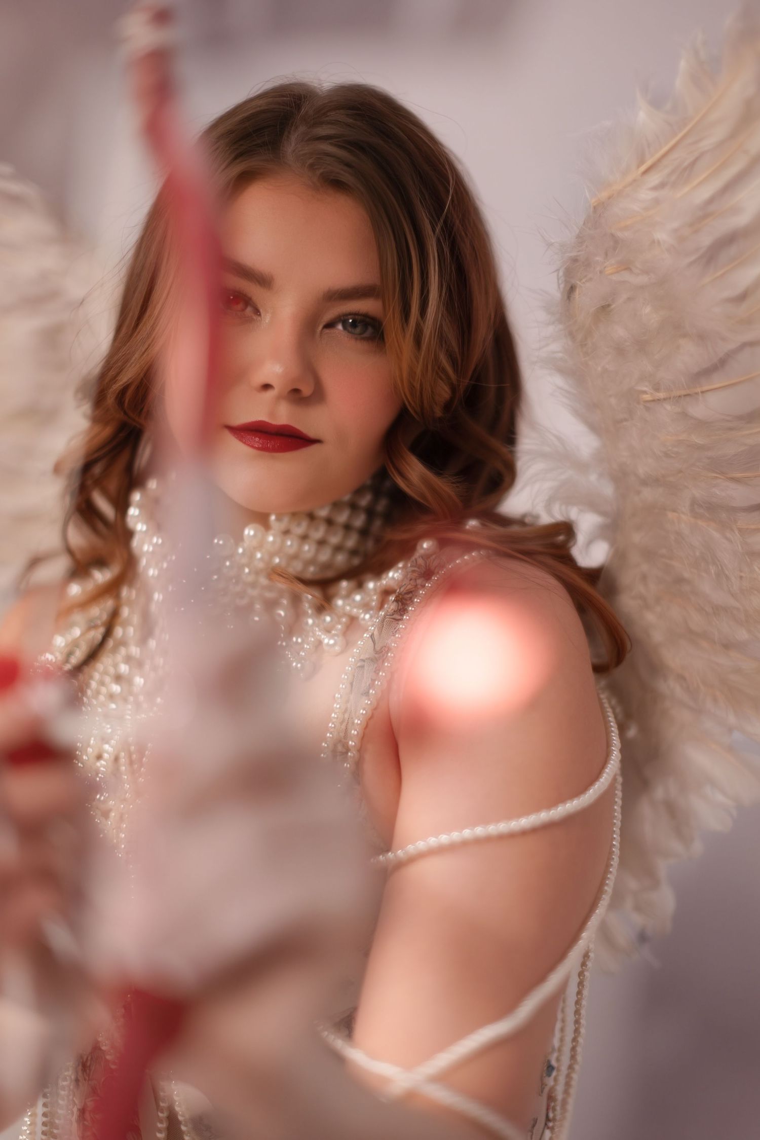 Dreamy boudoir photoshoot with angel wings, pearls, and soft pink lighting creating an ethereal Valentine's Day atmosphere.