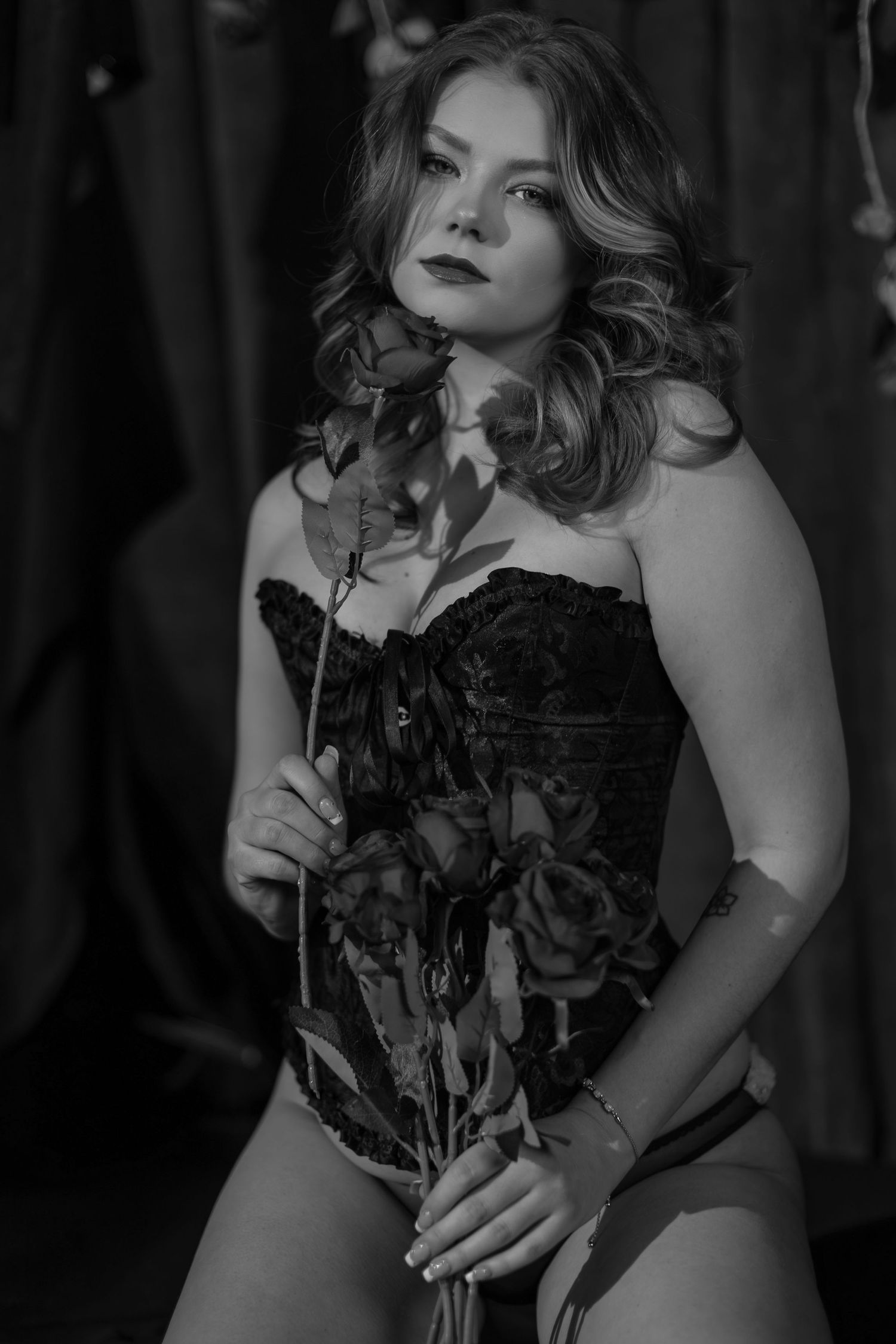 Dramatic black and white boudoir portrait with roses and corset in a moody studio setting.