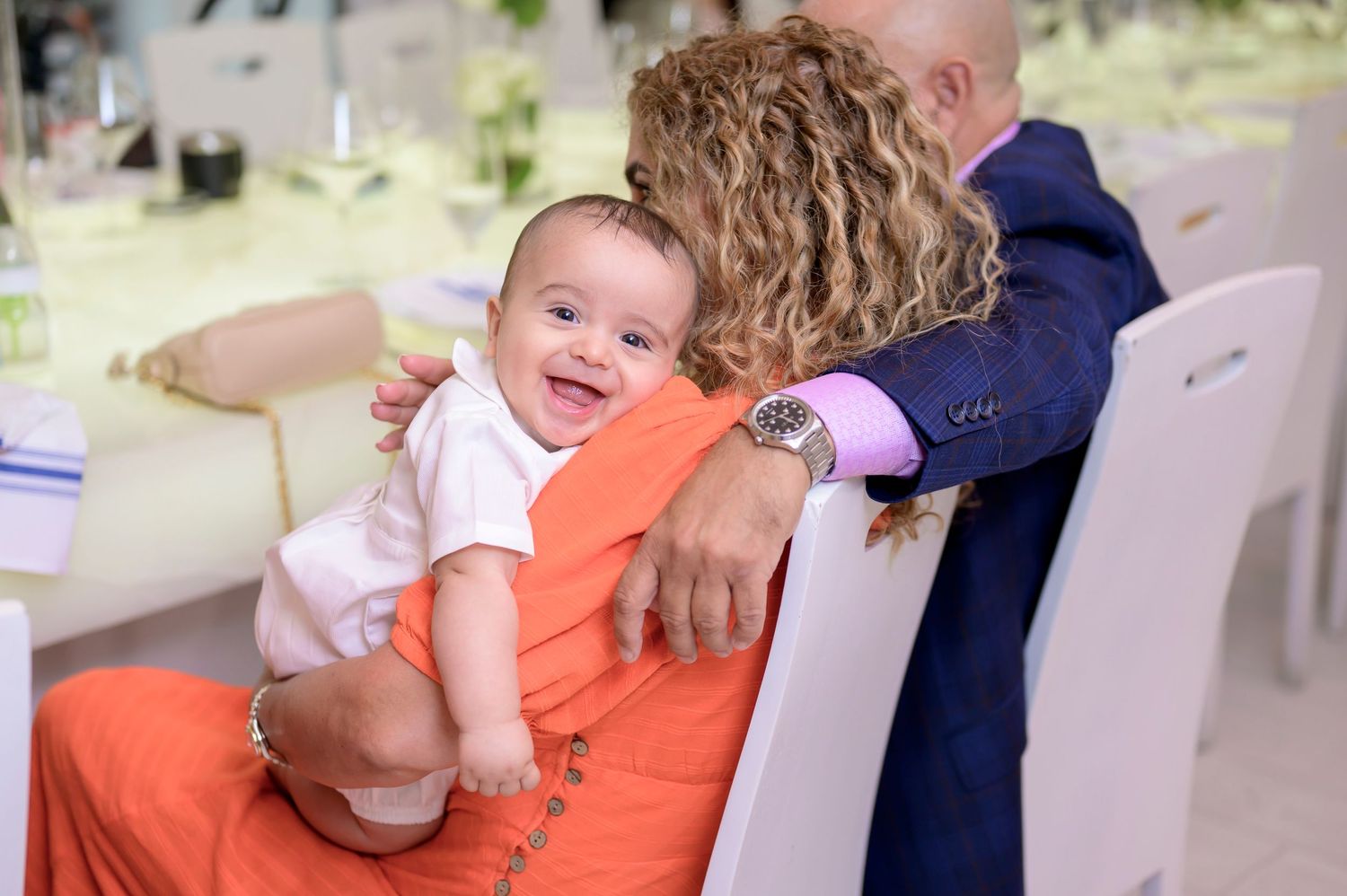 A happy infant wearing sits on someone's lap during an event.