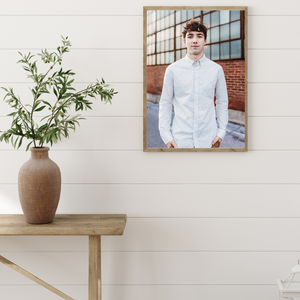 Portrait in wooden frame of person in white button-down shirt against brick wall with plant decor.