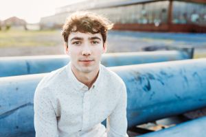 Portrait of senior high boy in white button-down shirt sitting by blue industrial equipment.