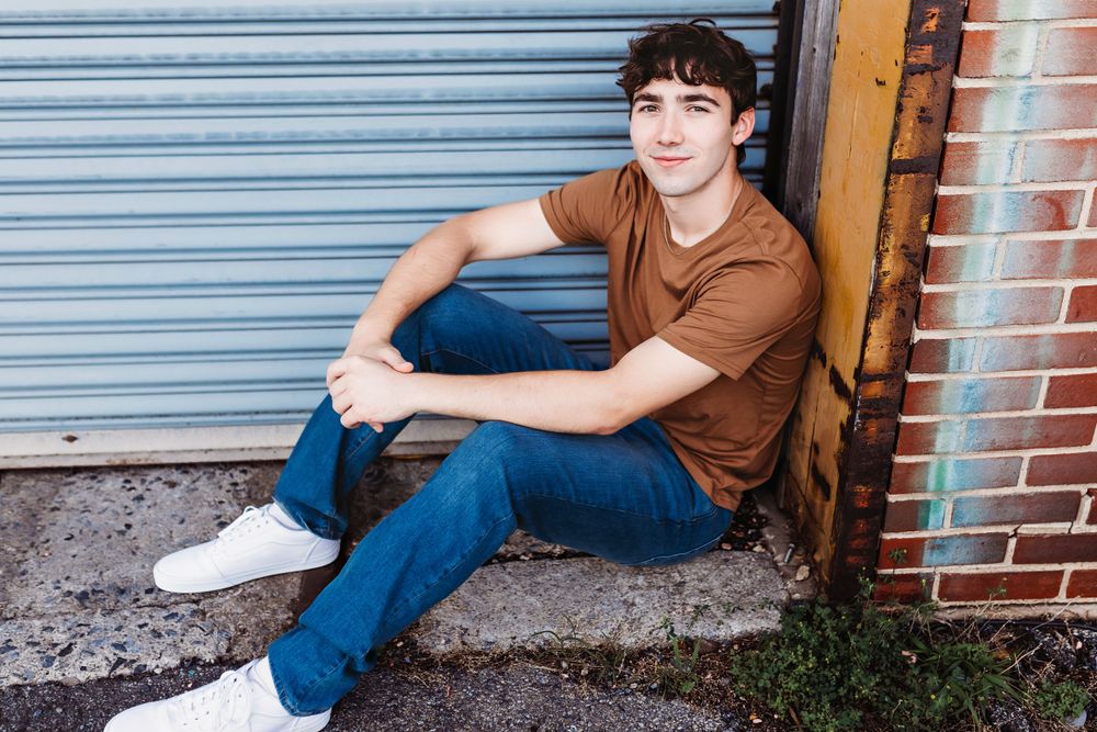 Person in brown shirt and jeans sitting casually against industrial doorway.