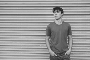 Black and white portrait of person in t-shirt against corrugated metal background.