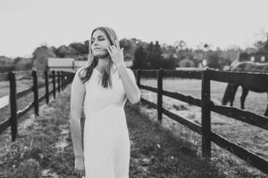 Black and white portrait of person in white dress standing by wooden fence.