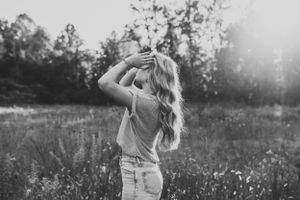 Black and white portrait of person with long hair in sunny meadow.