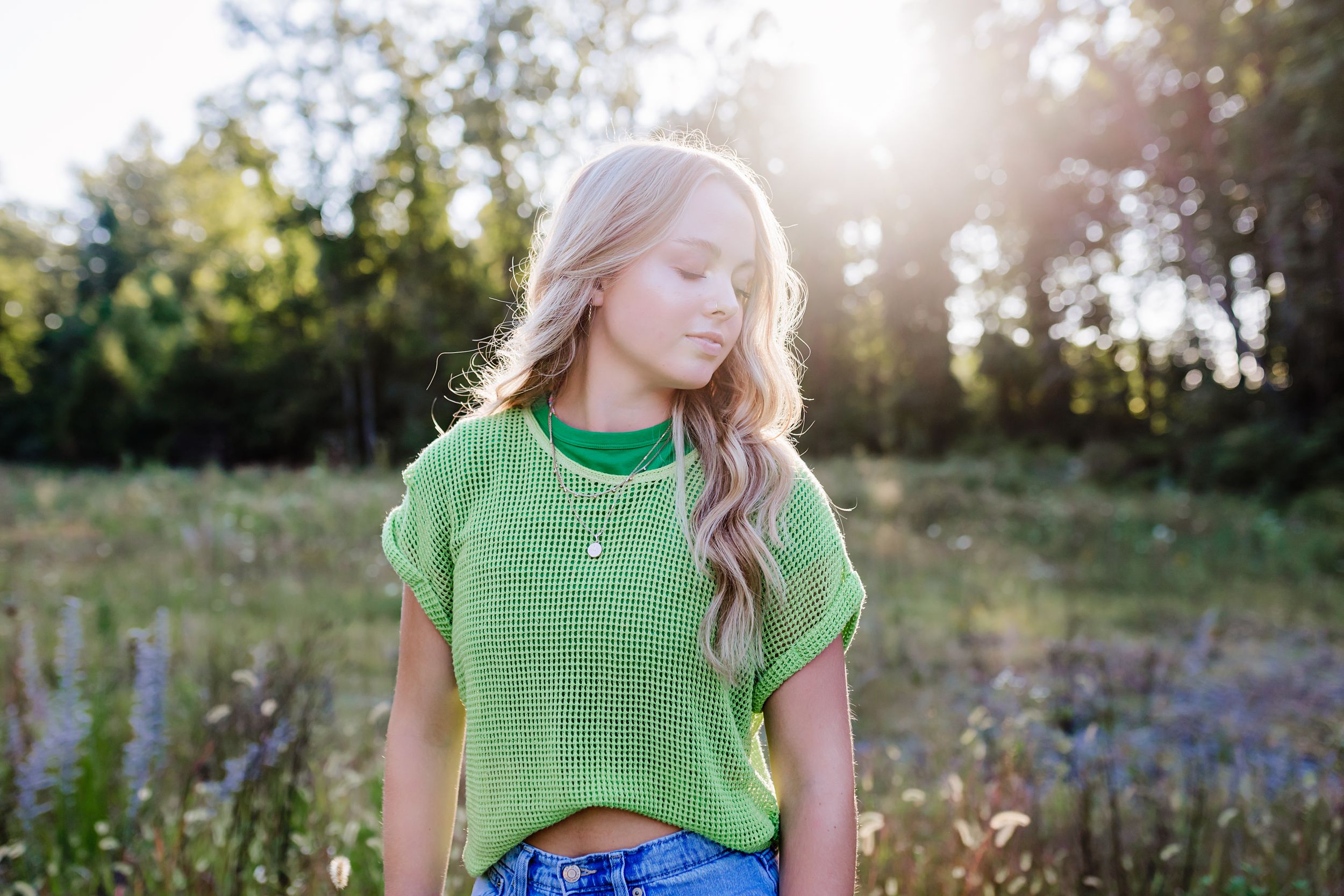 Person in bright green mesh top posing in summer field at sunset.
