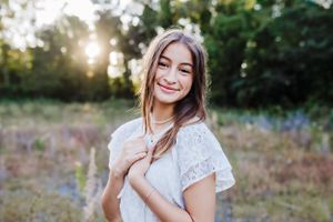 Portrait of someone in a white lace dress standing in a field at sunset with natural lighting.
