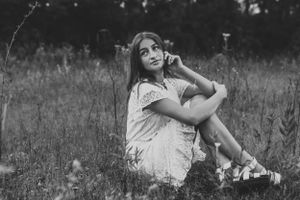 Black and white portrait of someone sitting in a field wearing a light dress.