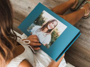 Person holding a blue photo album while sitting on wooden flooring.