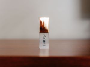 White skincare product bottle with copper metallic cap displayed on wooden surface.