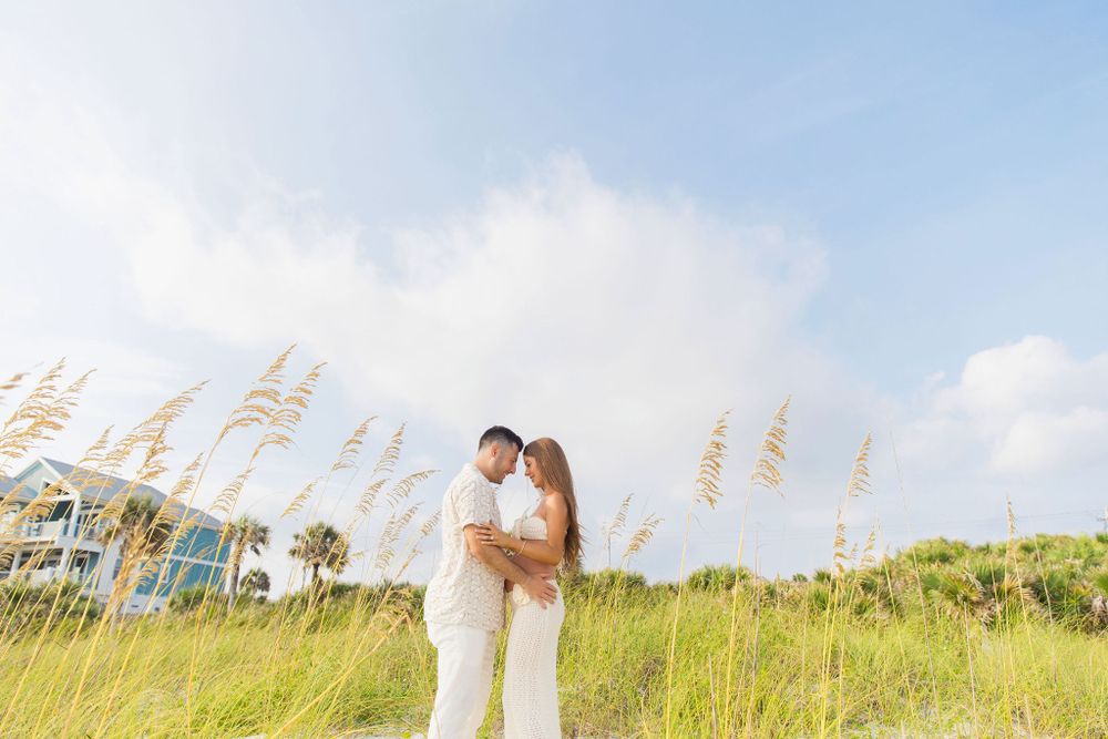 Couple embracing in field of tall sea oats with ocean in background.
