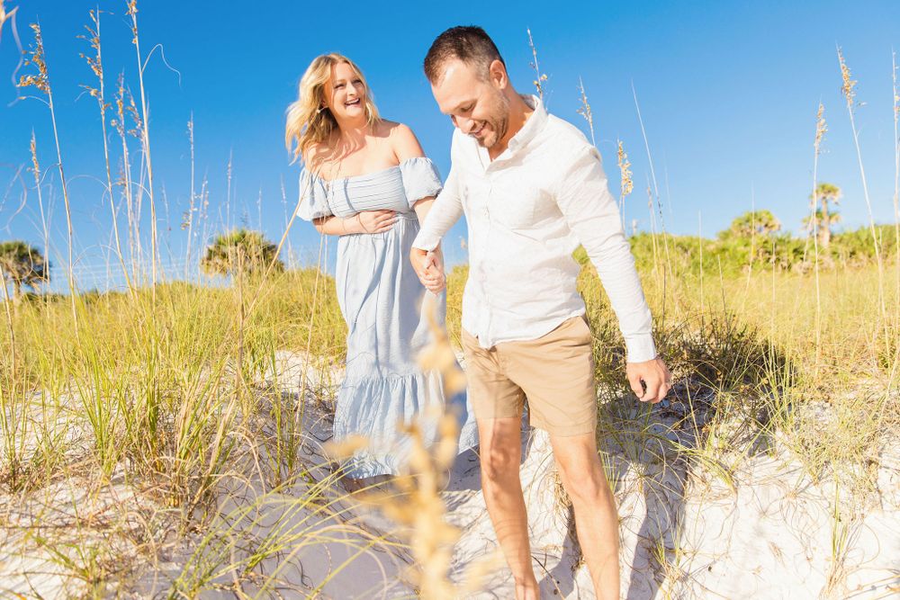 Couple walking through coastal dunes on sunny day.
