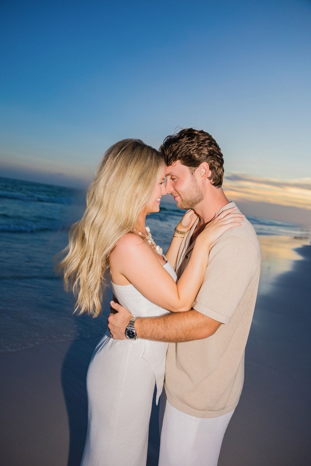 Romantic couple shares tender moments at sunset on a beach with ocean backdrop.