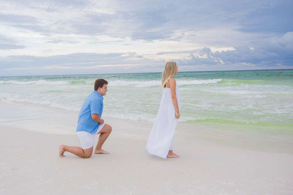A romantic beach proposal scene unfolds with turquoise waves and white sand creating a beautiful backdrop.