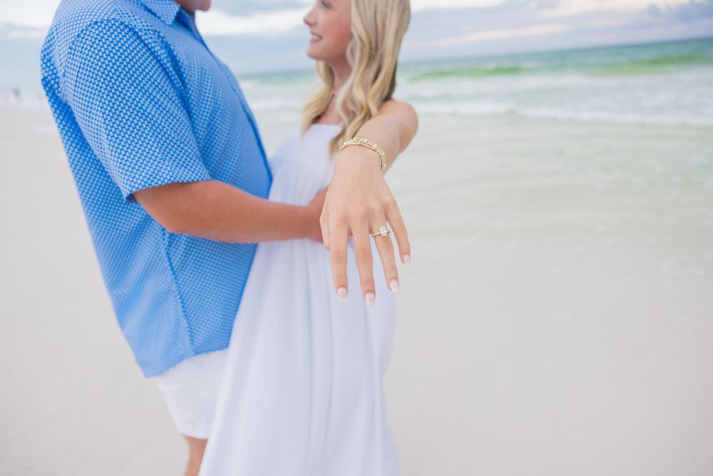 A couple in coordinating blue and white outfits walks hand in hand along a sandy beach at sunset.