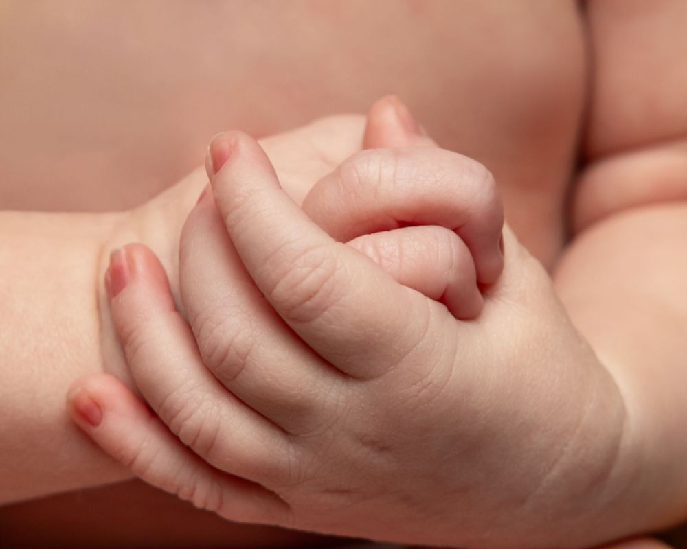 Close-up of a baby's tiny hands clasped together, showing delicate fingers and soft skin.