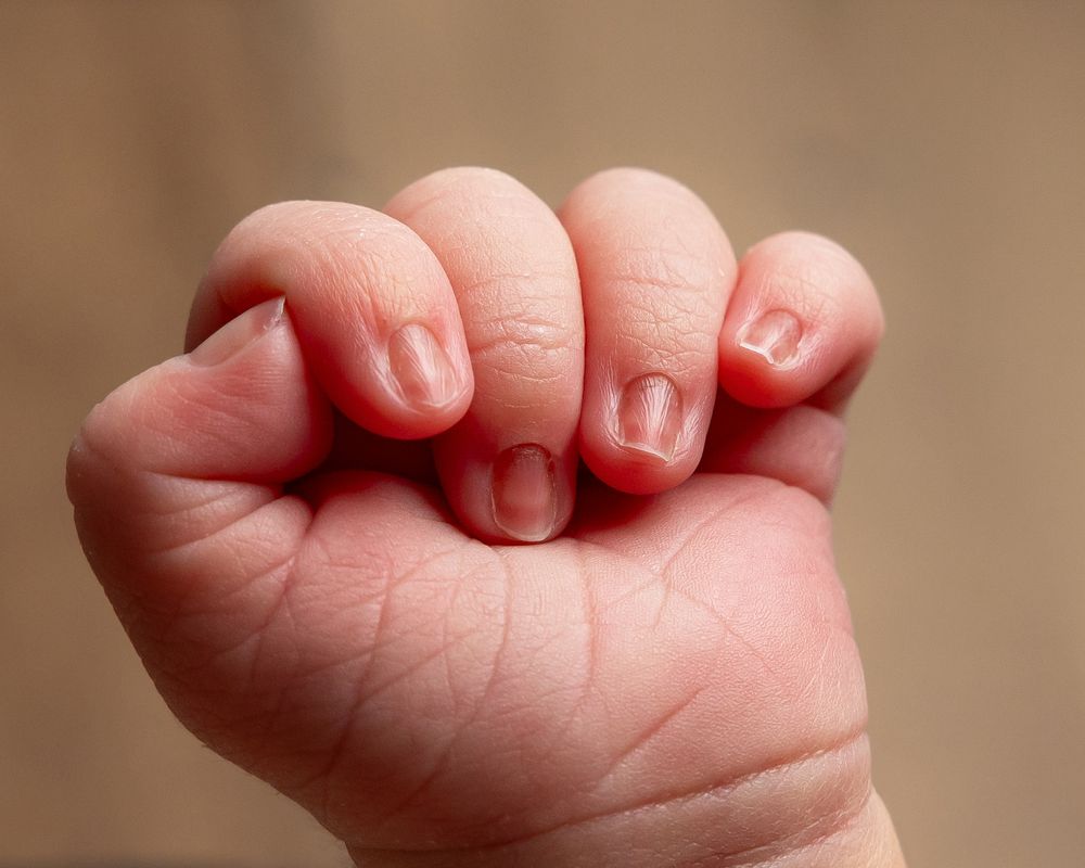 Close-up of a baby's tiny clenched fist showing delicate pink fingers and small fingernails.