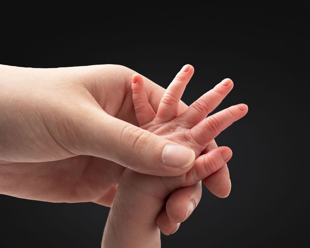 Close-up of two hands, one massaging the palm and fingers of the other against a dark background.