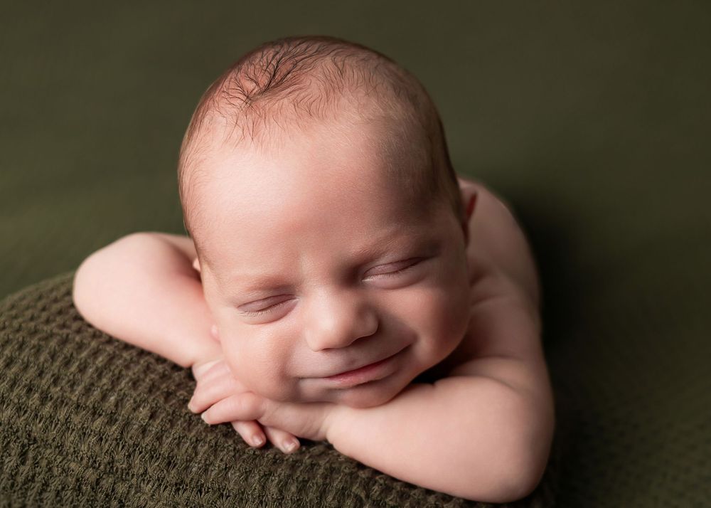 A sleeping newborn baby rests peacefully olive green blanket in a professional portrait setting. Newborn Photographer in Knoxville.