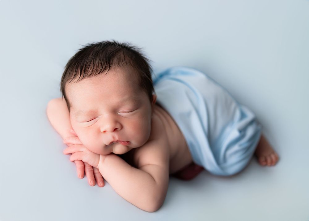 Peaceful newborn baby sleeping on a light blue background, wrapped in a soft blue blanket.